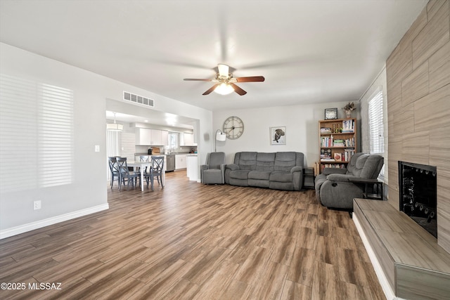 living room featuring ceiling fan, a tiled fireplace, and hardwood / wood-style floors