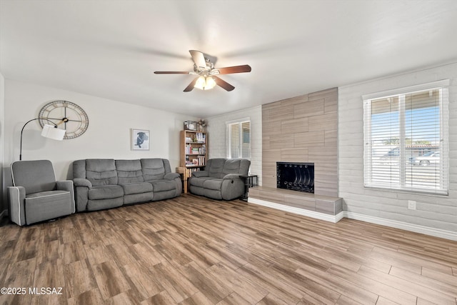 living room featuring hardwood / wood-style flooring, ceiling fan, and a tiled fireplace