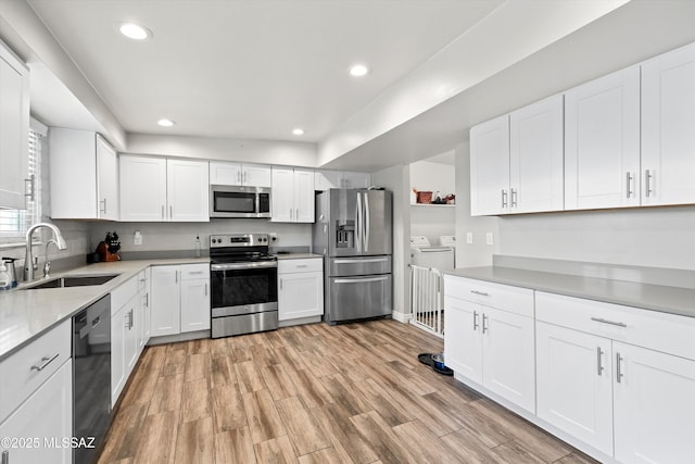 kitchen with independent washer and dryer, appliances with stainless steel finishes, sink, and white cabinets