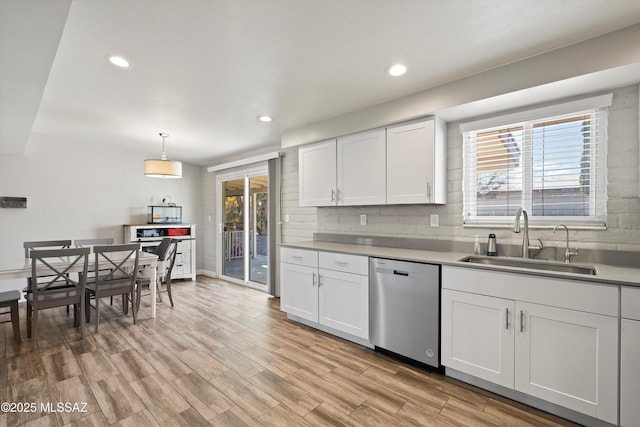 kitchen with pendant lighting, sink, white cabinets, stainless steel dishwasher, and a healthy amount of sunlight