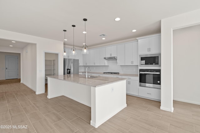 kitchen featuring appliances with stainless steel finishes, sink, white cabinets, a kitchen island with sink, and light stone countertops