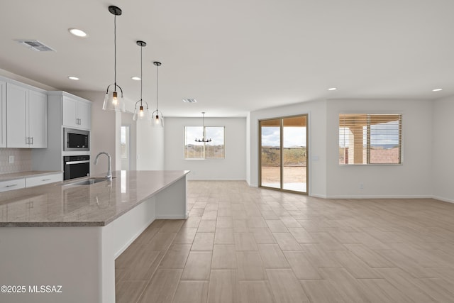 kitchen with sink, stainless steel microwave, pendant lighting, oven, and white cabinets