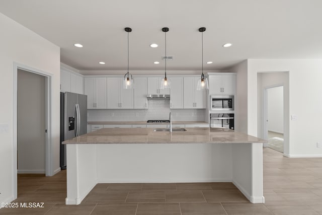 kitchen with appliances with stainless steel finishes, an island with sink, white cabinets, hanging light fixtures, and light stone countertops