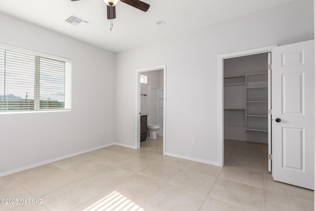 unfurnished bedroom featuring ceiling fan, connected bathroom, light tile patterned flooring, a spacious closet, and a closet