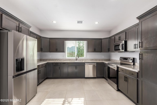 kitchen with stainless steel appliances, dark brown cabinets, sink, and light stone counters