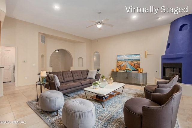 living area featuring visible vents, a ceiling fan, arched walkways, a large fireplace, and light tile patterned flooring