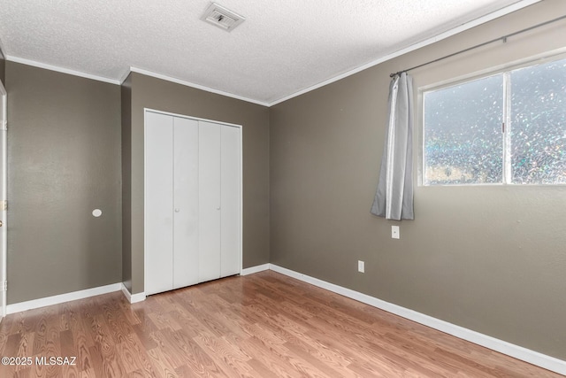 unfurnished bedroom with ornamental molding, a closet, a textured ceiling, and light wood-type flooring