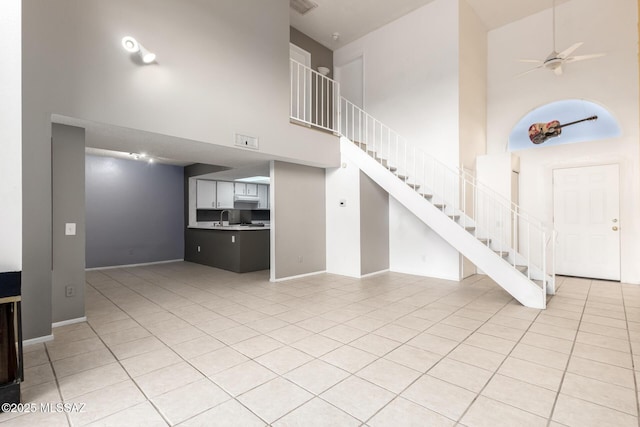 unfurnished living room featuring ceiling fan, a towering ceiling, sink, and light tile patterned floors