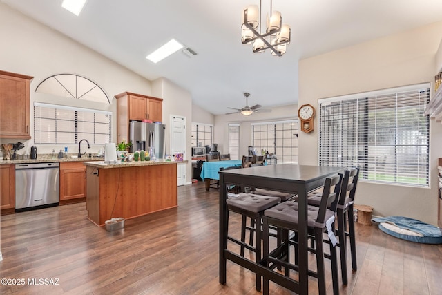 kitchen featuring decorative light fixtures, lofted ceiling, a center island, light stone counters, and stainless steel appliances