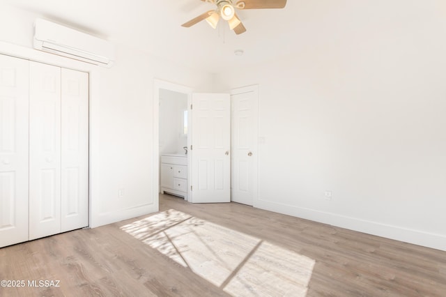 unfurnished bedroom with an AC wall unit, connected bathroom, light hardwood / wood-style flooring, ceiling fan, and a closet