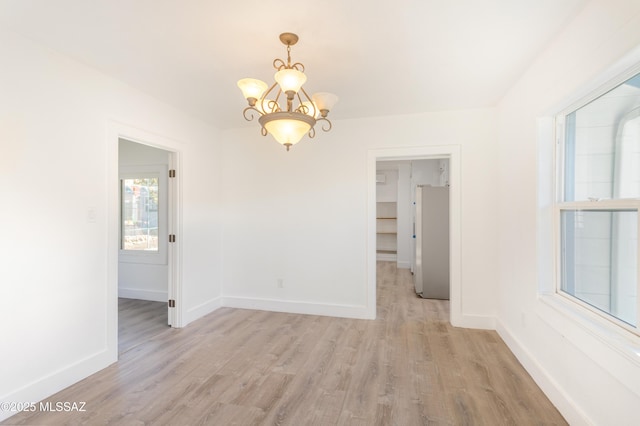 spare room with an inviting chandelier and light hardwood / wood-style flooring