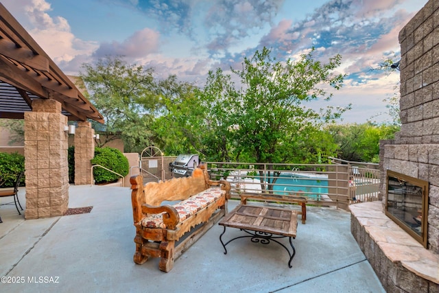 patio terrace at dusk with area for grilling, a grill, and an outdoor stone fireplace