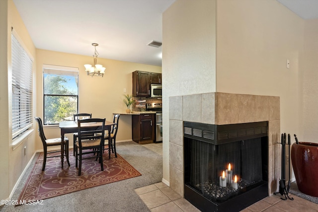 dining space featuring a tiled fireplace, light colored carpet, and a chandelier