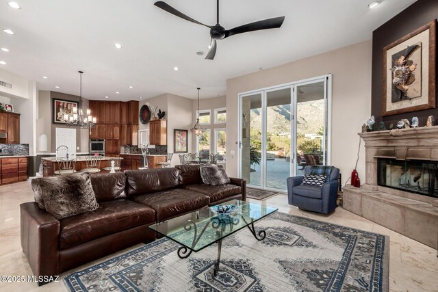 living room with a fireplace and ceiling fan with notable chandelier