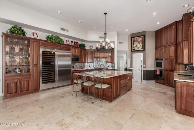 kitchen featuring pendant lighting, sink, appliances with stainless steel finishes, light stone counters, and an island with sink