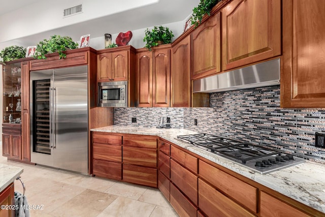 kitchen featuring light tile patterned floors, built in appliances, light stone counters, and decorative backsplash