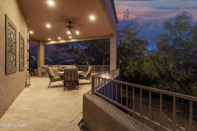 patio terrace at dusk featuring ceiling fan and an outdoor kitchen