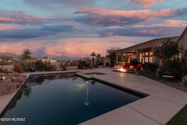 pool at dusk featuring an in ground hot tub, a fire pit, and a patio area