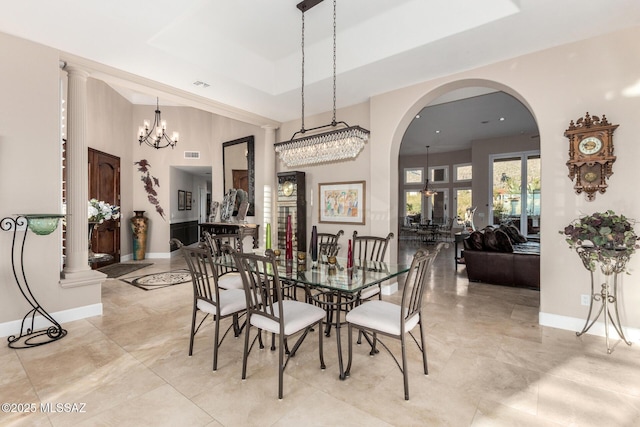 dining space with a high ceiling, a tray ceiling, a notable chandelier, and ornate columns