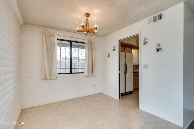 spare room with brick wall, a chandelier, and a textured ceiling