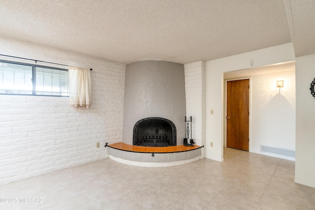 unfurnished living room with brick wall, a textured ceiling, and a fireplace