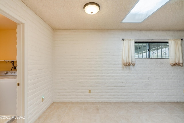 tiled empty room with washer / dryer, a skylight, and a textured ceiling