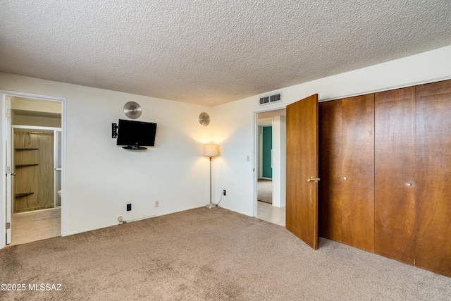 unfurnished bedroom with a closet, connected bathroom, light carpet, and a textured ceiling