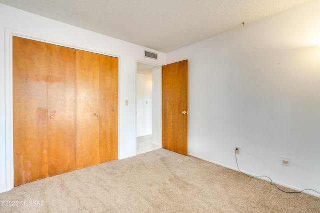 unfurnished bedroom featuring light colored carpet, a textured ceiling, and a closet