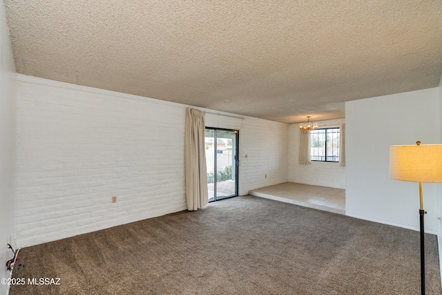 carpeted empty room with brick wall, a notable chandelier, and a textured ceiling