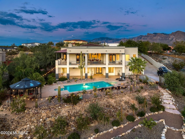 back house at dusk with a fenced in pool, a gazebo, a patio, a mountain view, and a balcony