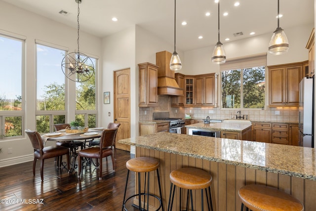 kitchen with stainless steel appliances, hanging light fixtures, backsplash, and light stone counters