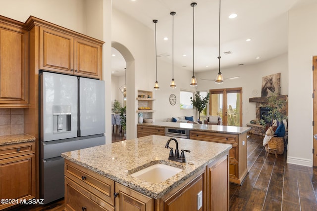 kitchen with sink, white refrigerator with ice dispenser, hanging light fixtures, and a center island with sink