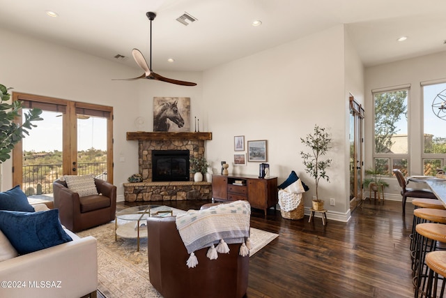 living room featuring dark wood-type flooring, ceiling fan, and a stone fireplace