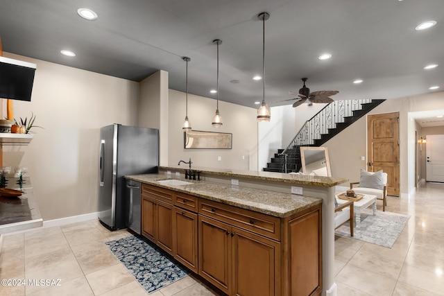 kitchen with pendant lighting, sink, appliances with stainless steel finishes, light stone counters, and kitchen peninsula