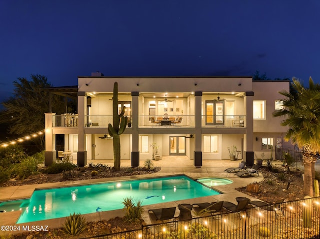 back house at twilight with ceiling fan, a patio area, a fenced in pool, and a balcony