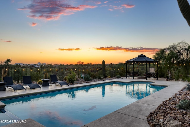 pool at dusk with a gazebo and a patio area