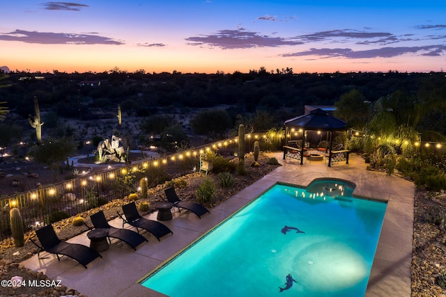 pool at dusk with a gazebo and a patio area