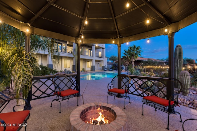 pool at dusk featuring a gazebo, a patio, and a fire pit