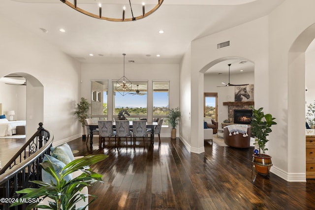 dining space featuring dark hardwood / wood-style flooring, a stone fireplace, ceiling fan with notable chandelier, and a wall unit AC