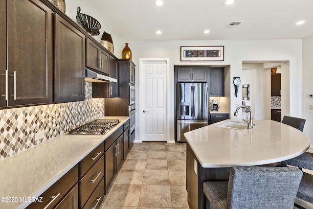 kitchen with sink, a breakfast bar, appliances with stainless steel finishes, a center island with sink, and decorative backsplash