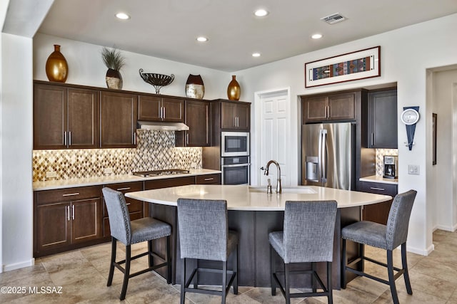 kitchen with stainless steel appliances, a breakfast bar area, a center island with sink, and backsplash