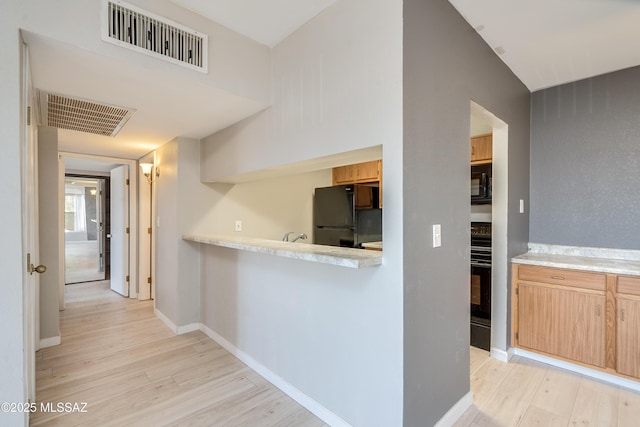 kitchen with light brown cabinetry, light hardwood / wood-style floors, and black appliances