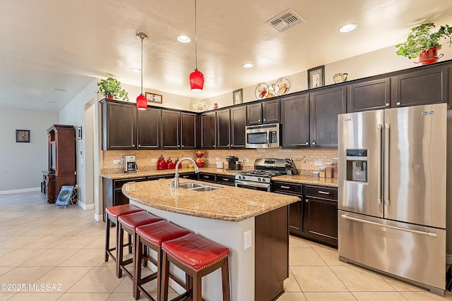 kitchen with sink, light stone counters, decorative light fixtures, an island with sink, and stainless steel appliances