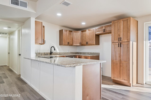 kitchen featuring light wood-type flooring, sink, light stone counters, and kitchen peninsula