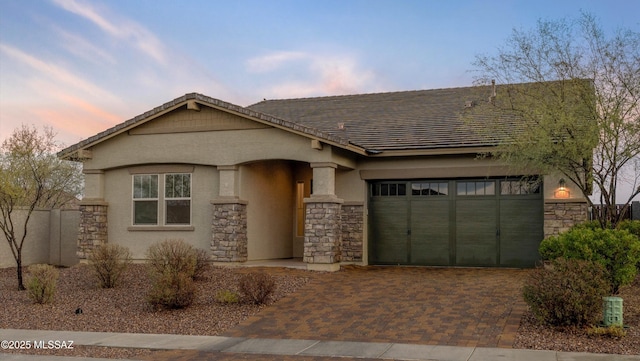 view of front of property featuring an attached garage, a tile roof, stone siding, decorative driveway, and stucco siding