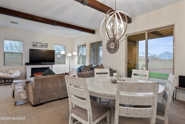 carpeted dining space with visible vents, a mountain view, a chandelier, beamed ceiling, and a lit fireplace