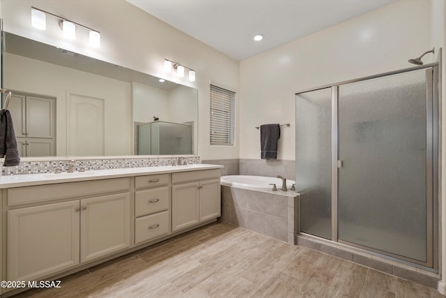 full bathroom with a sink, wood finished floors, a shower stall, a bath, and double vanity