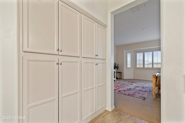 hallway with light carpet, visible vents, and baseboards