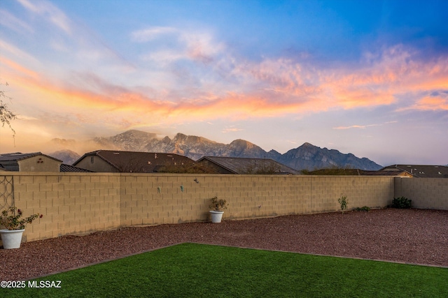 yard at dusk featuring a fenced backyard and a mountain view