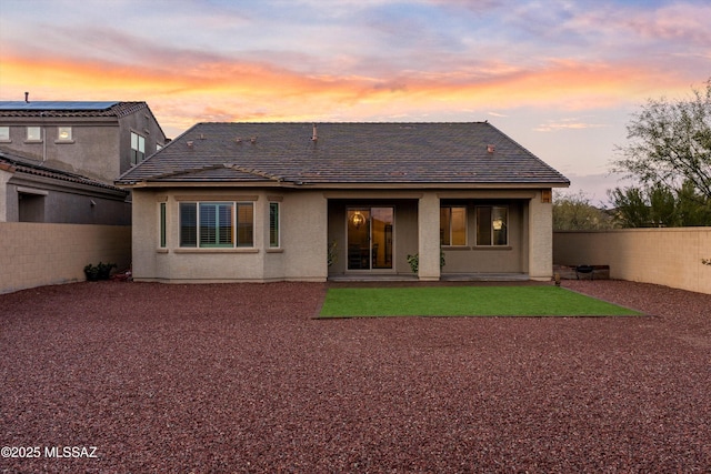 back of property at dusk with a tile roof, fence, and stucco siding